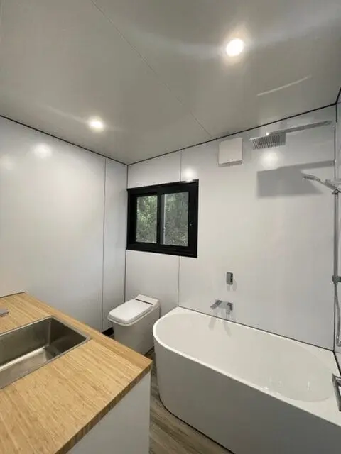 A freestanding bath and toilet in a MicroHome bathroom, with a window above the vanity.