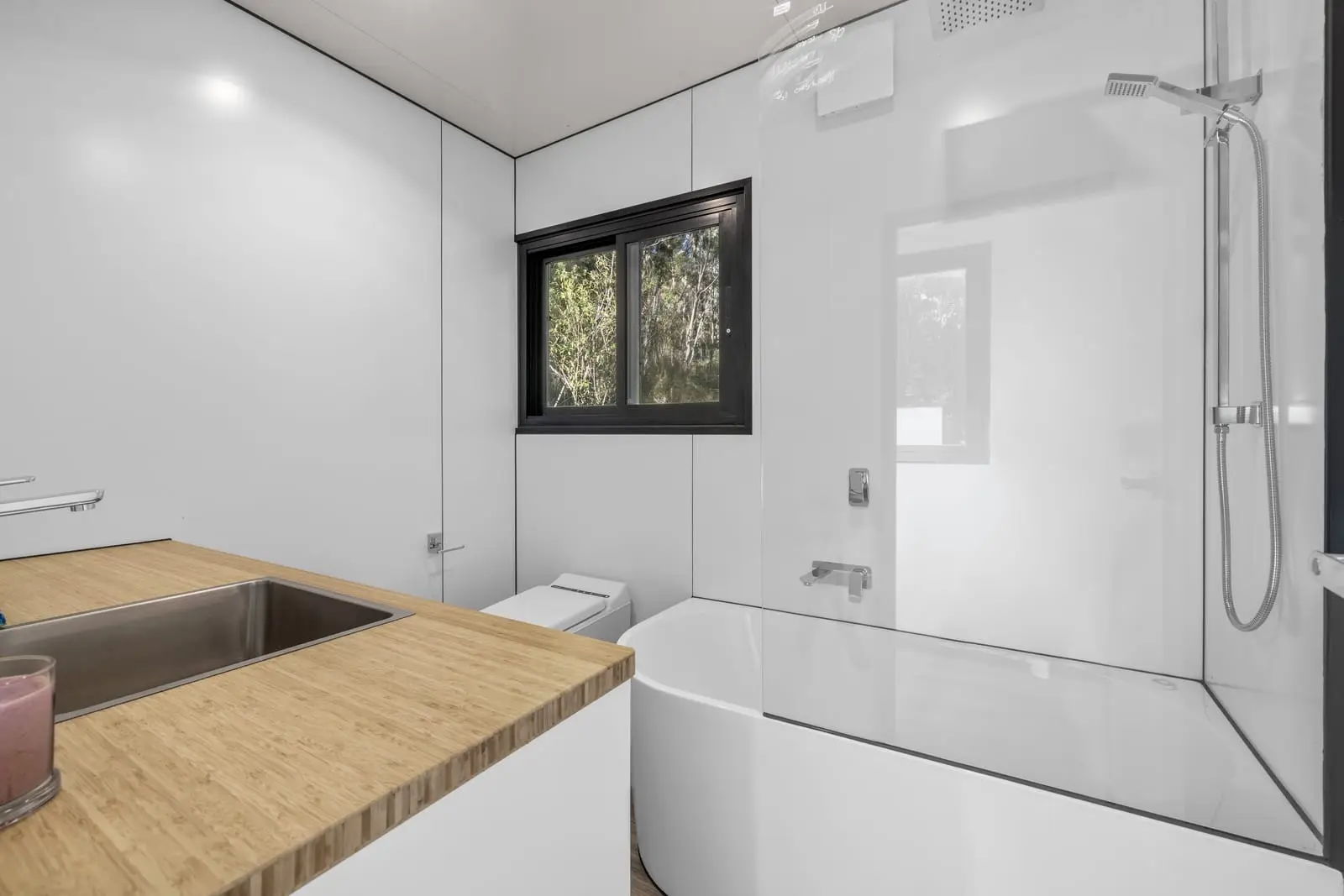 The bathroom of a finished MicroHome, with a full-size bath, a separate shower and a timber-topped vanity.