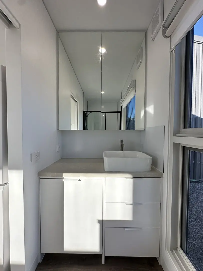 A MicroHome bathroom vanity with a bowl basin, drawers below, a mirrored cabinet above and a window beside it.