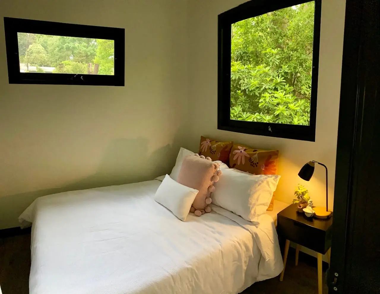 A made bed beside a MicroHome window looking out into green bushland.
