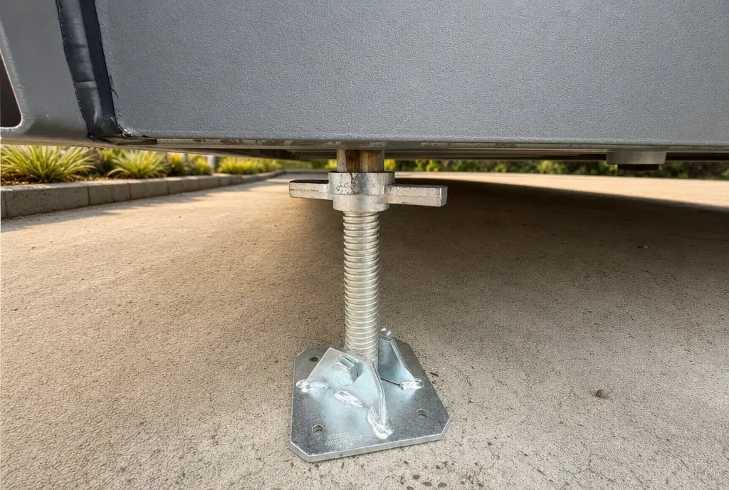 A galvanised levelling leg under the steel chassis of a MicroHome, with the low underside clear of the ground — play the chassis build walkthrough