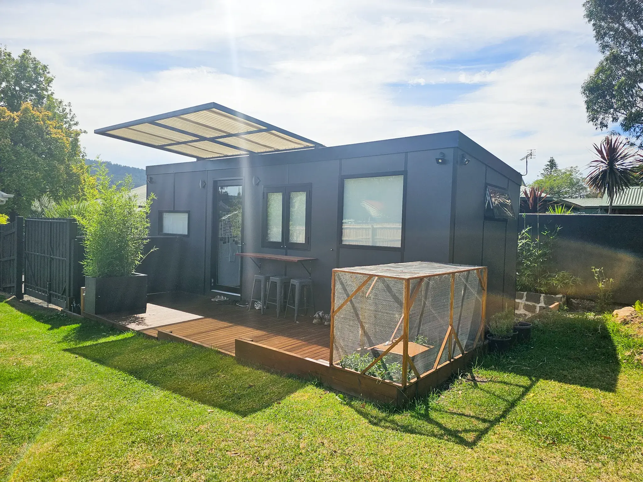 Daniel Kloppenborg’s charcoal-clad MicroHome in a backyard, with a cantilevered awning over a timber deck and a raised veggie garden.