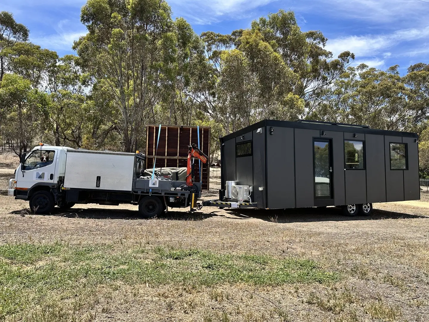 A charcoal MicroHome being towed behind the MicroHomes truck onto a rural site.
