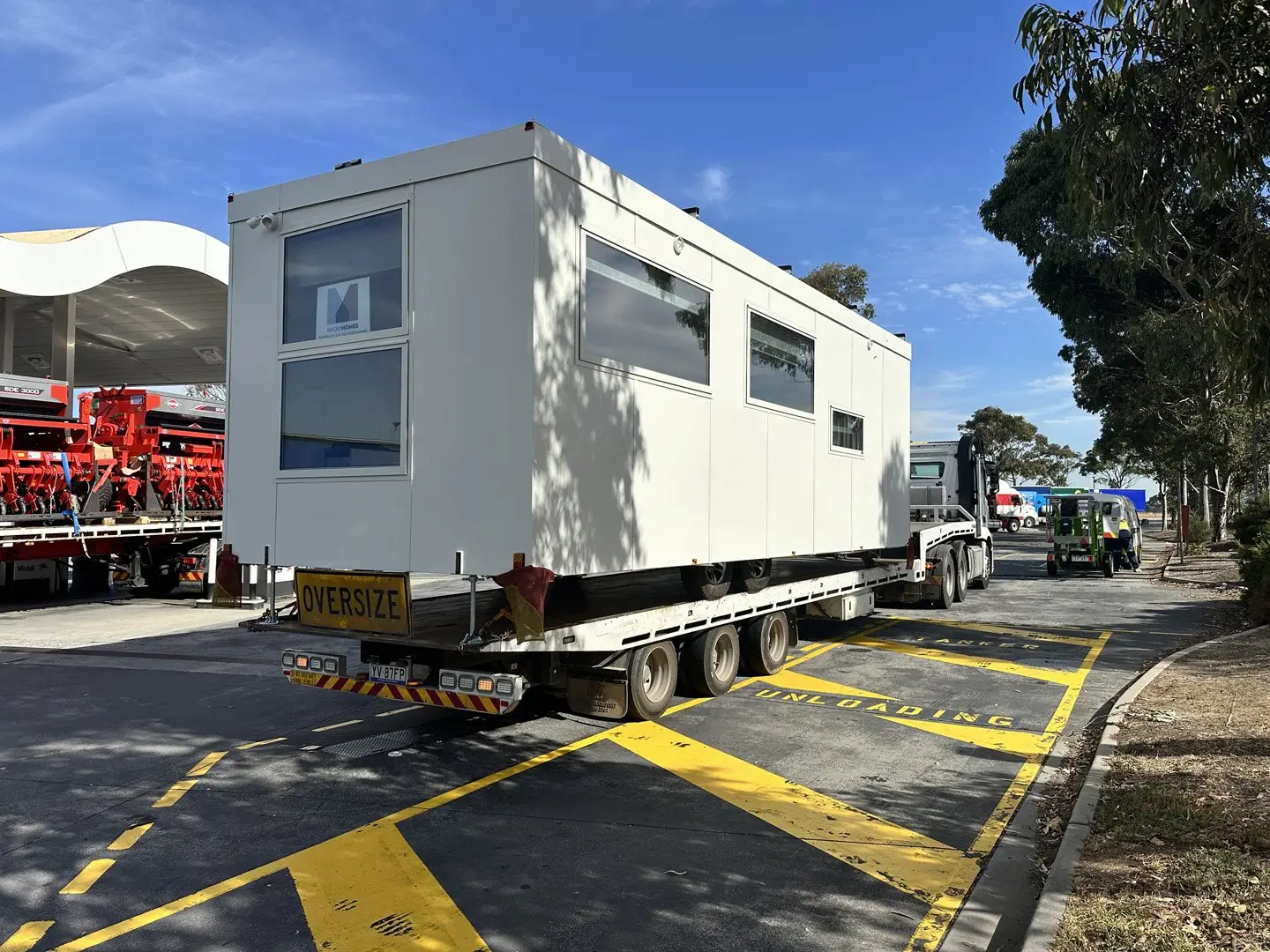 A white MicroHome travelling on a multi-axle flatbed with an OVERSIZE sign on the rear.
