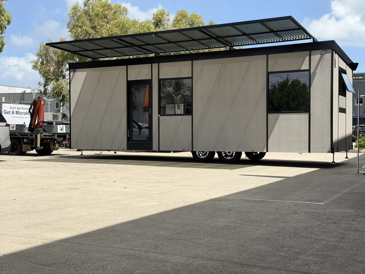 A grey-clad MicroHome on its wheels in the factory yard, its solar awning raised over the roof.