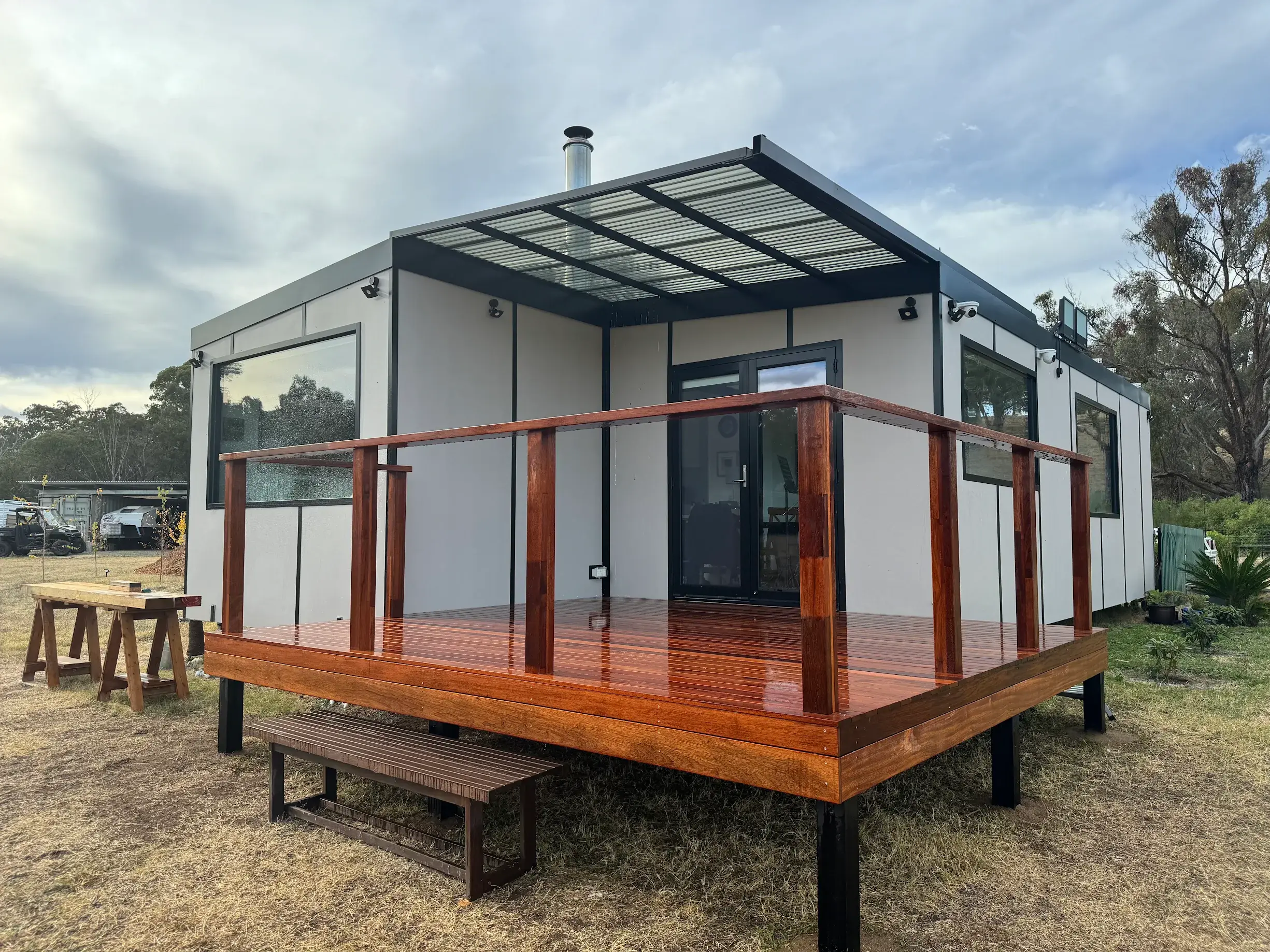 Heather James’s finished MicroHome on open country, with a glossy hardwood deck and glass balustrade.