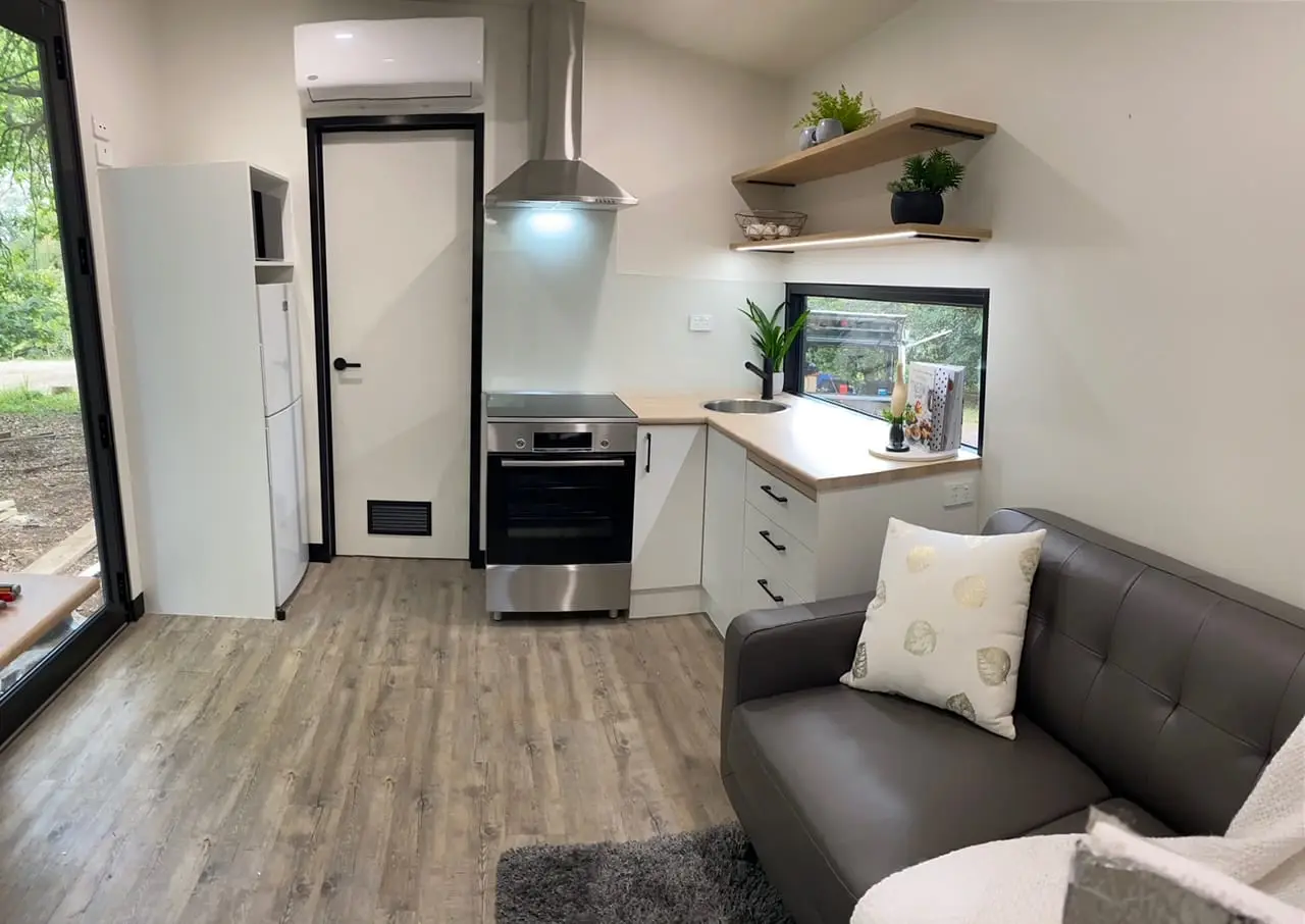 A MicroHome kitchen with an oven and rangehood, opening straight onto the lounge.