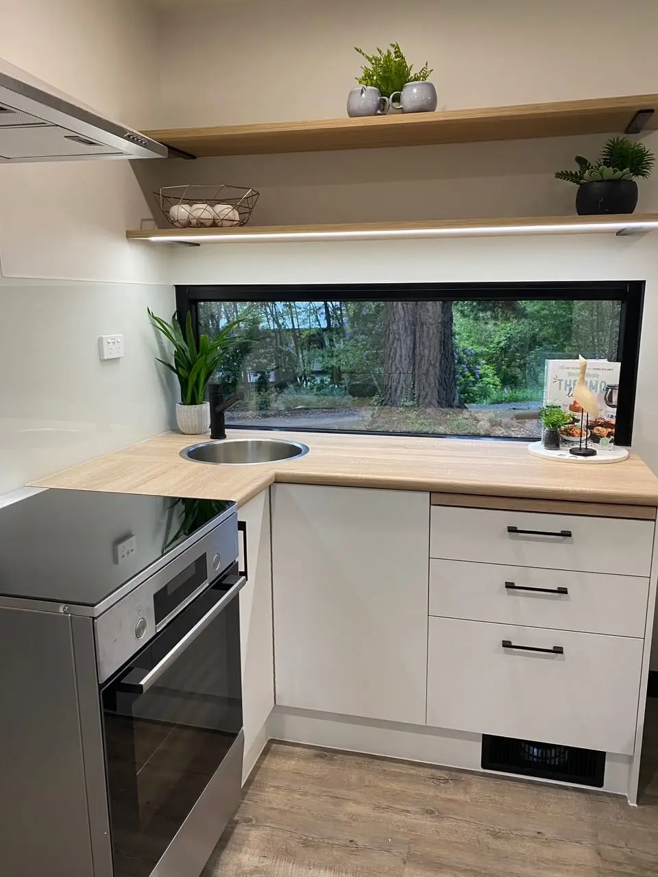 A MicroHome kitchen bench with a full-size oven, drawer cabinetry and a sink under the window.