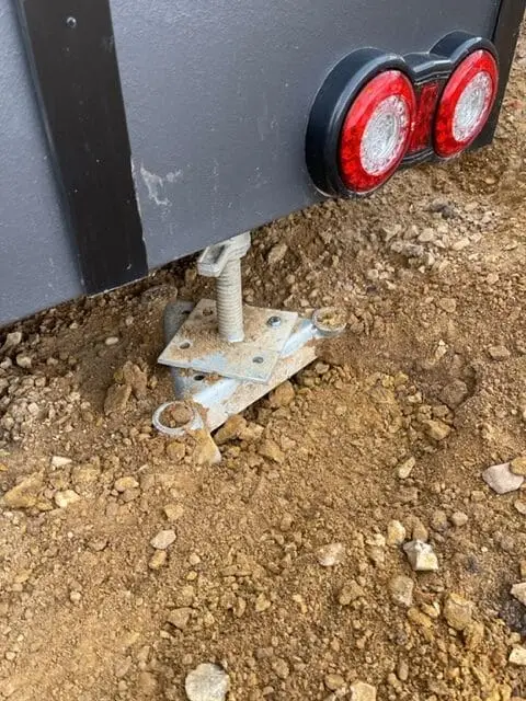 An adjustable levelling leg and tail-light detail under the rear corner of a sited MicroHome.