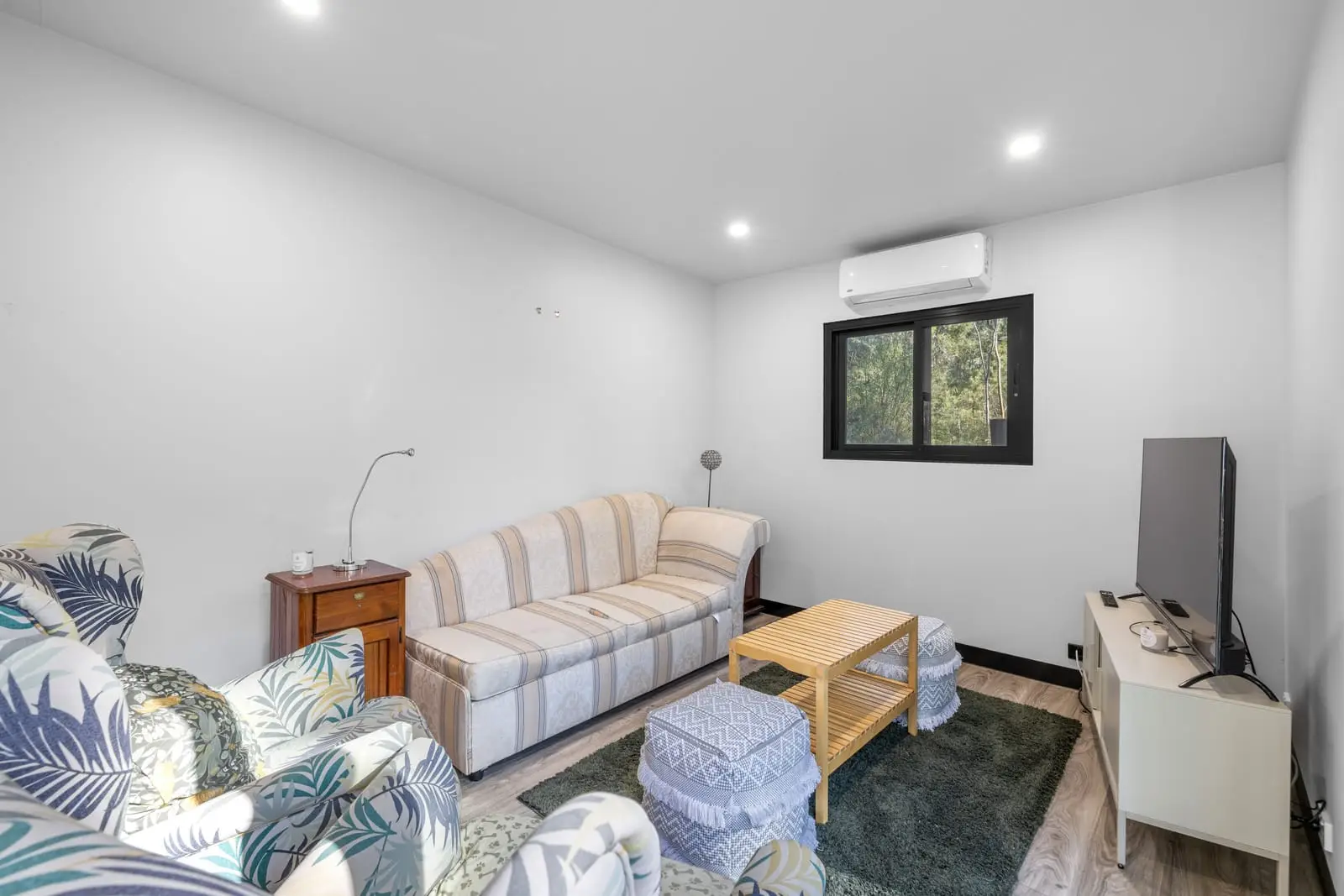 The other end of the same living room, with a sofa, side table and a window onto the trees.