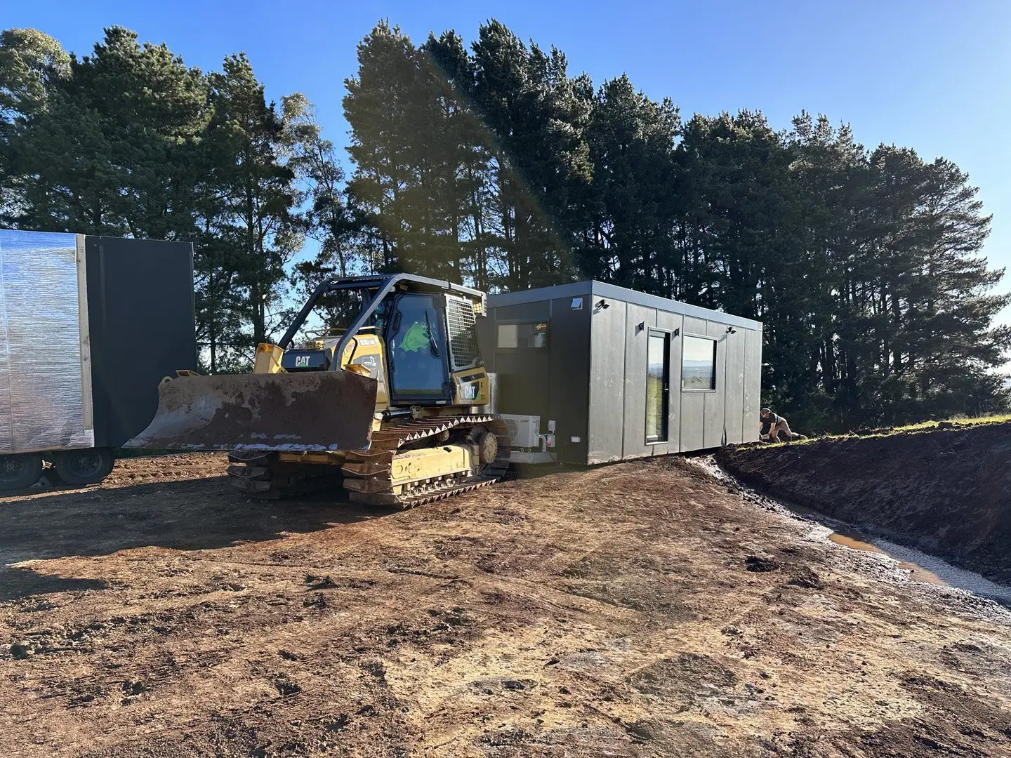 A dozer placing a MicroHome on a prepared pad, with a second unit waiting beside it.