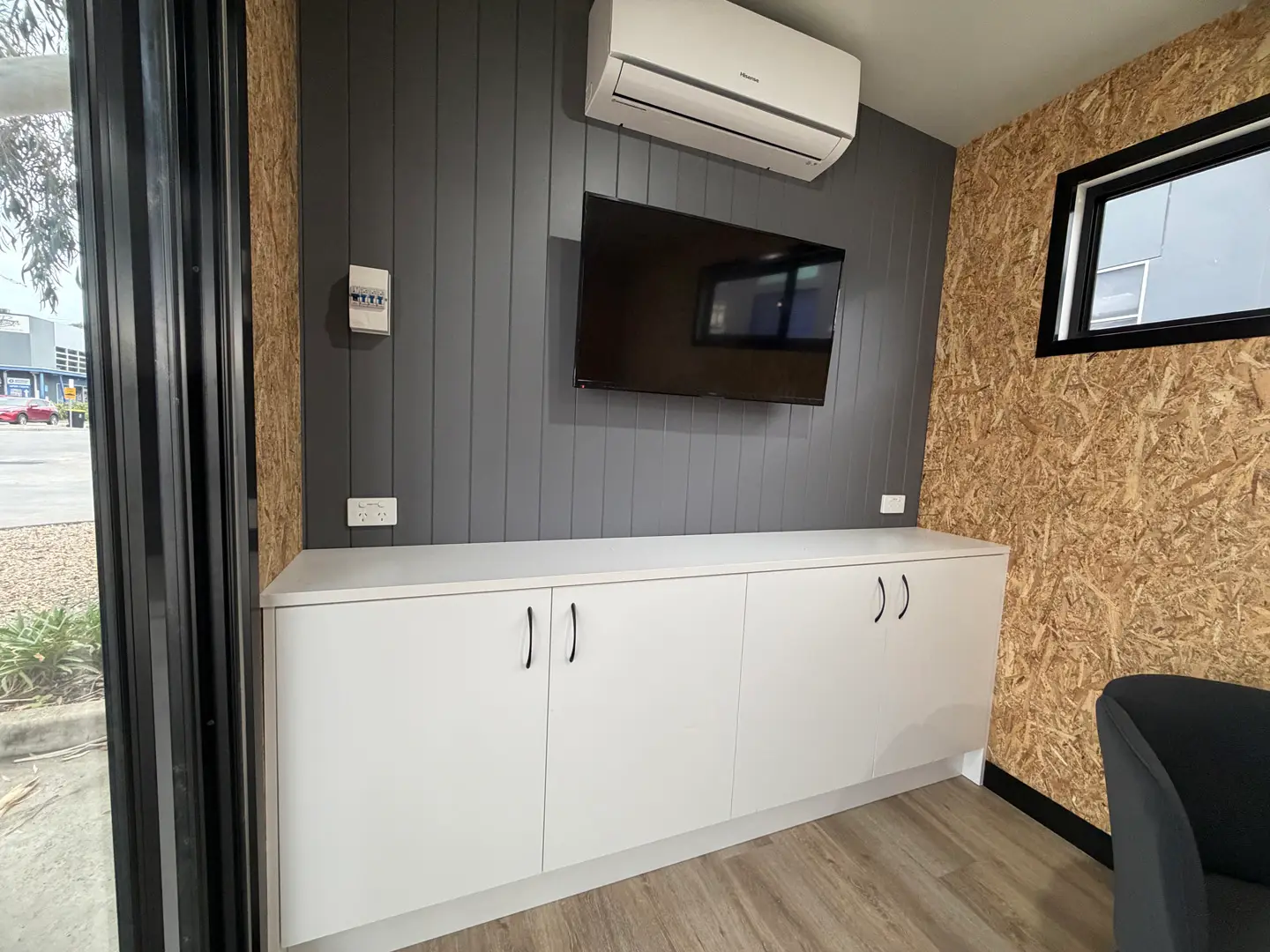 White built-in cabinetry beneath a wall-mounted TV and split-system air conditioner inside the ex-demo Backyard Pod.
