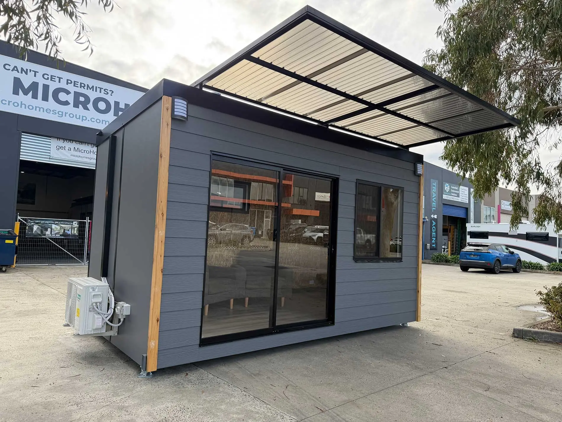 A Backyard Pod outside the MicroHomes factory in Melbourne, clad in blue and timber with a steel awning over the entry.