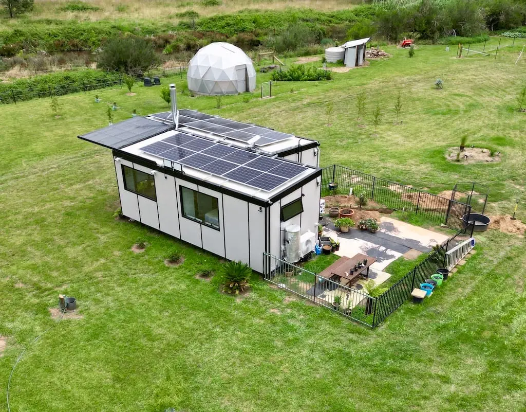 A MicroHome standing in an open paddock, roof panels visible along its length.