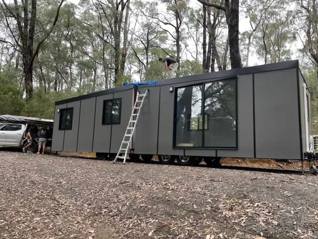 A MicroHome newly positioned on a gravel pad in bushland, ladder against the side.