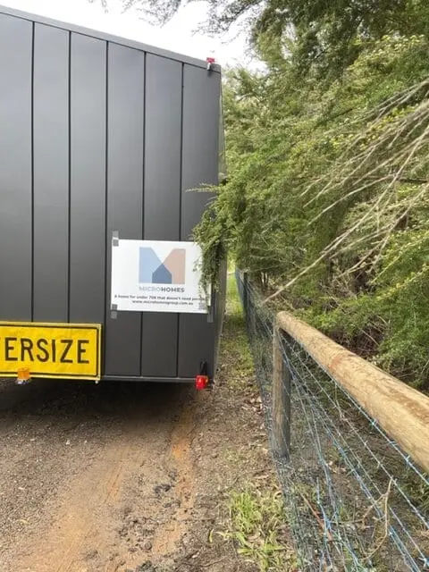 The rear of a MicroHome under tow on a bush track, OVERSIZE sign and MicroHomes plate visible.