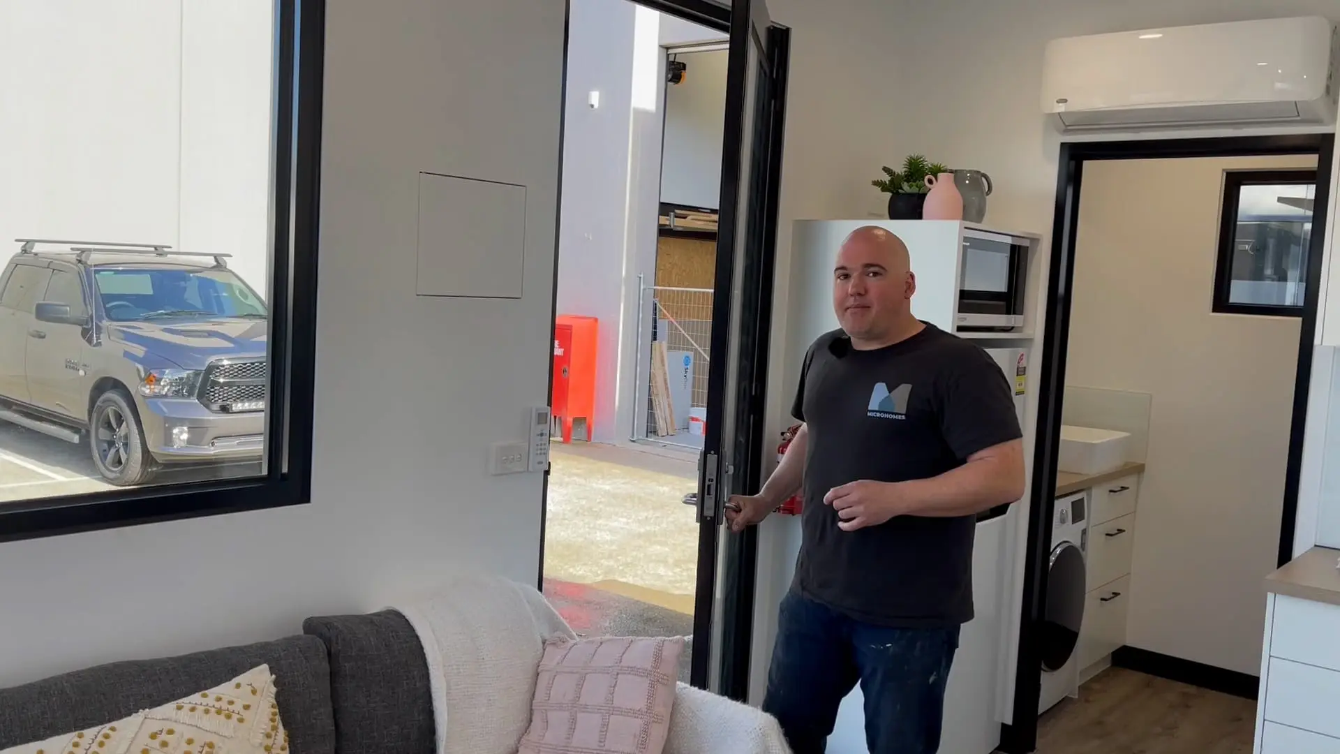 A MicroHomes team member in the doorway of a home under fit-out, commercial-grade door and glazing installed.
