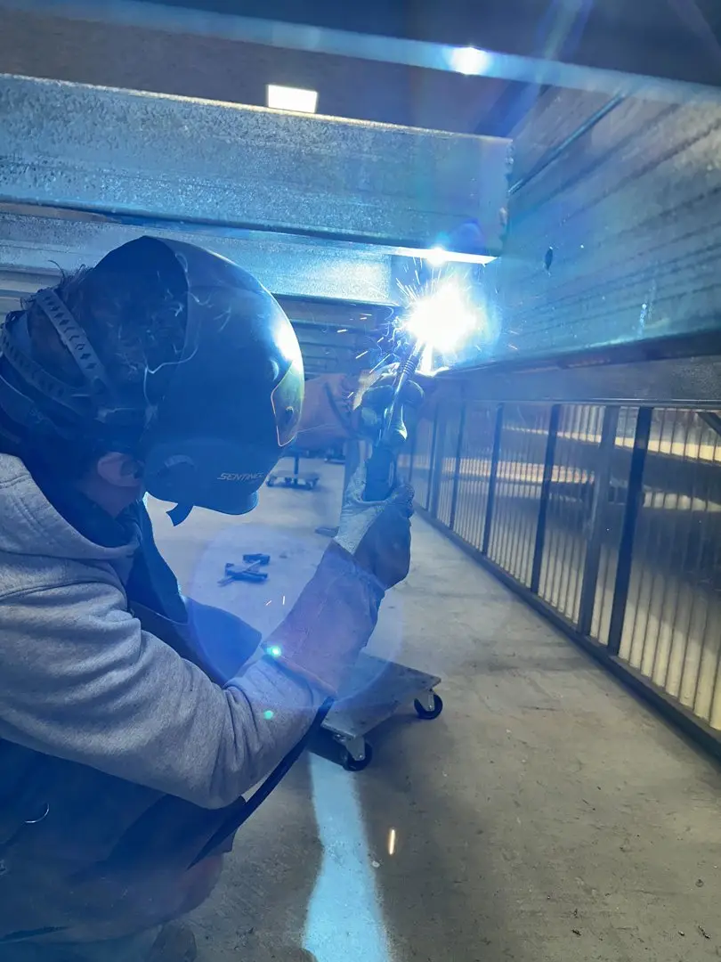 A welder in a helmet working on the steel underframe of a MicroHome at the factory.
